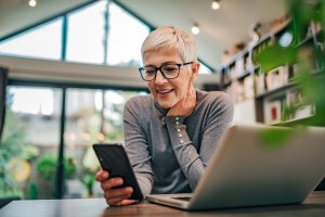 smiling mature woman at desk with phone and laptop